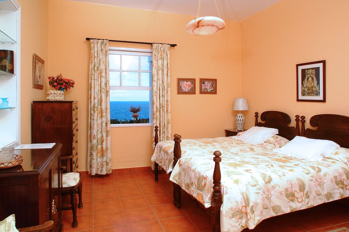 Une chambre à coucher avec un lit, un bureau, une chaise, une fenêtre avec des rideaux et une vue sur la mer.