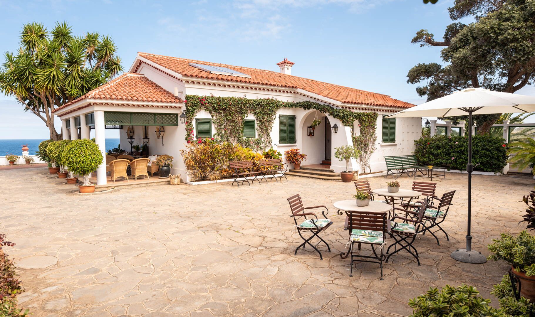 Une villa de style méditerranéen, dotée d’un toit en tuiles, d’un espace extérieur aménagé pour se détendre et de plantes en pot.