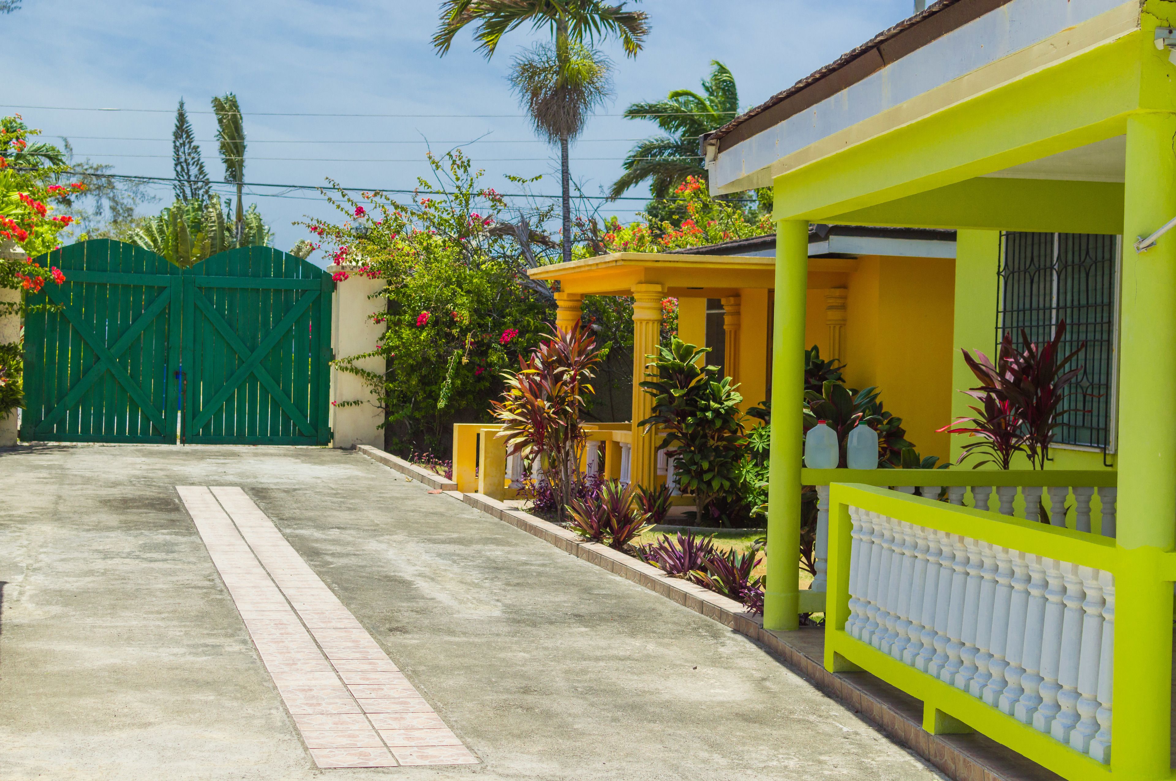 Una propiedad residencial con entrada protegida por un portón, un porche cubierto y un jardín bien cuidado con diversas plantas y flores.