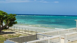 A beach view with clear turquoise water, a sandy shore, and a white building with a balcony. - Seacrest Beach Hotel (St. Ann's Bay)