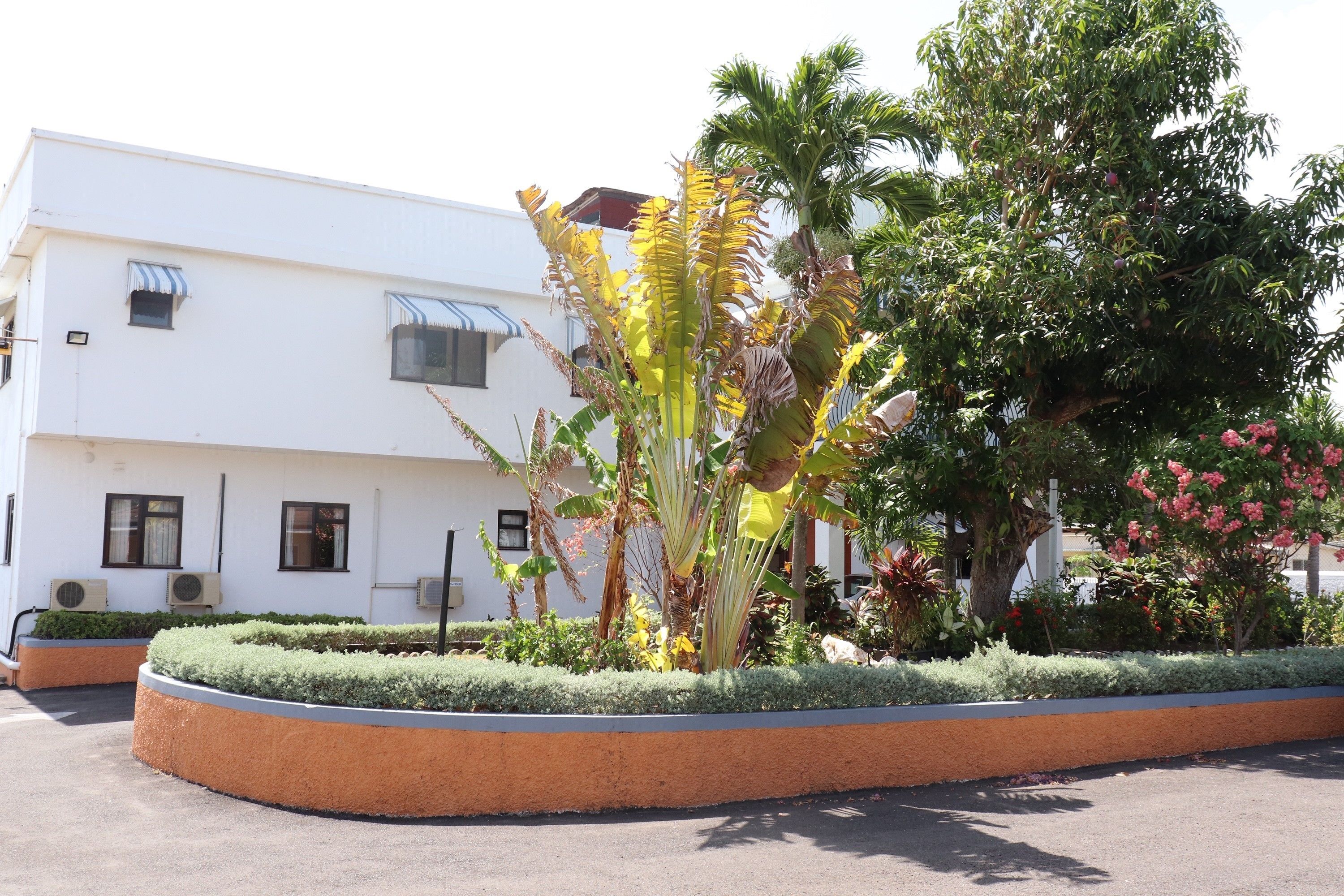 A building with a white exterior, air conditioning units, and a landscaped garden with various plants and a palm tree.