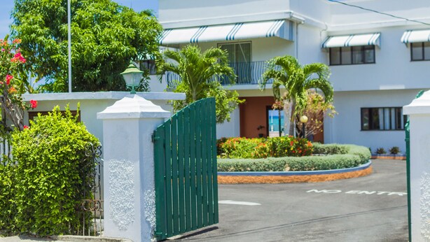 A multi-story hotel with a white facade, a green gate, and a landscaped garden area. - Seacrest Beach Hotel (St. Ann's Bay)