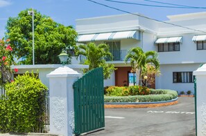 A multi-story hotel with a white facade, a green gate, and a landscaped garden area.