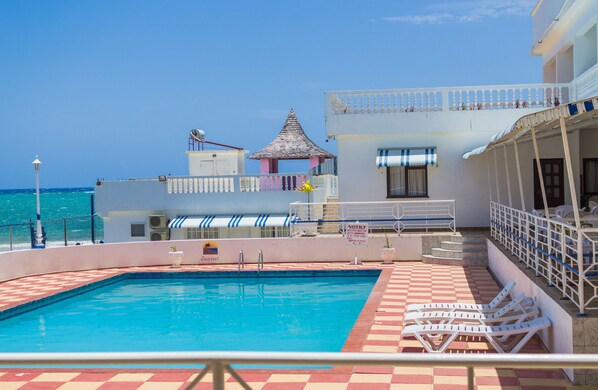 A swimming pool with lounge chairs, a view of the sea, and a building with a balcony.