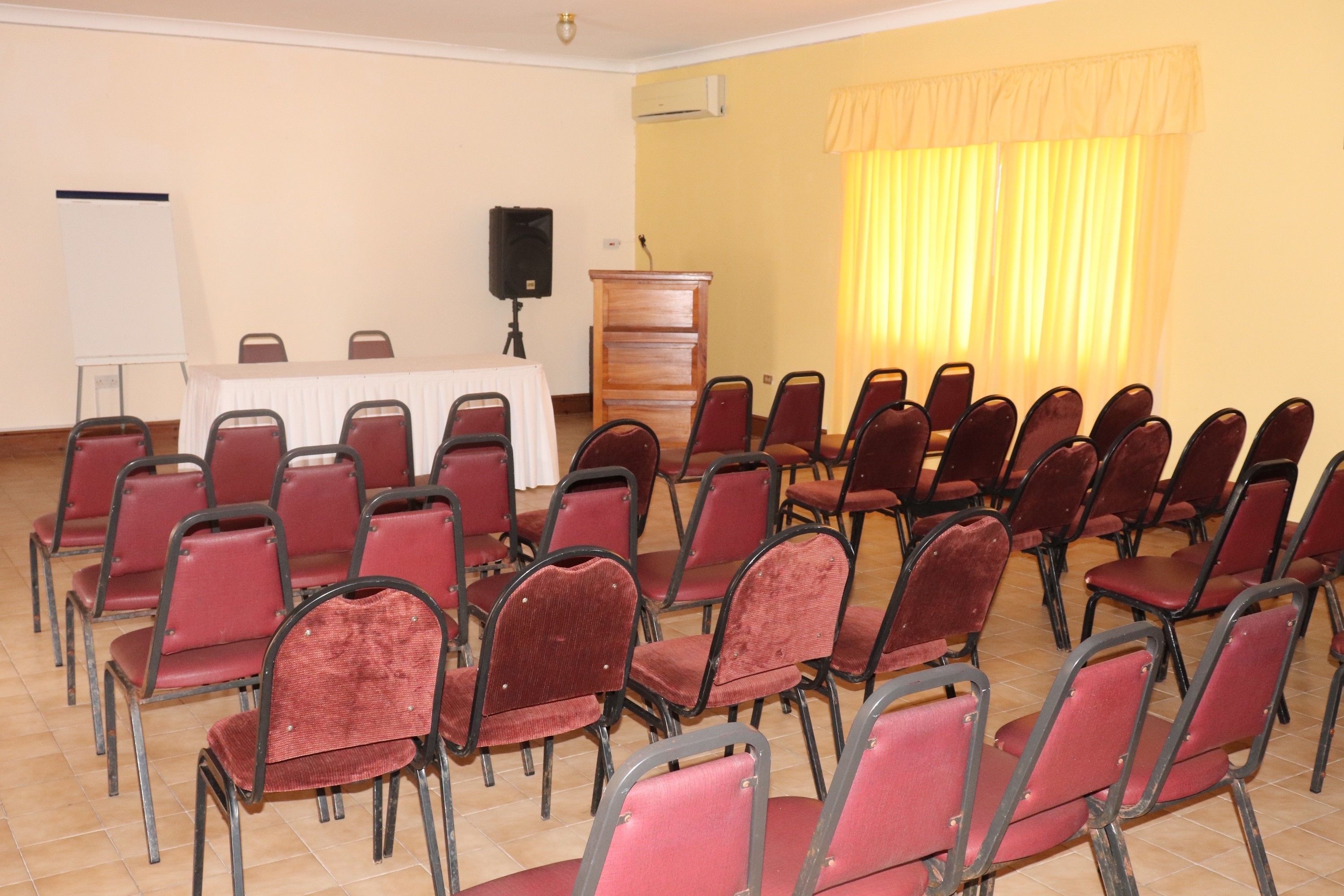Un salón de conferencias con filas de sillas rojas, una mesa blanca con un atril y un orador.