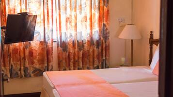 Habitación de hotel con cama, televisión instalada en la pared, lámpara y cortinas con estampado floral.