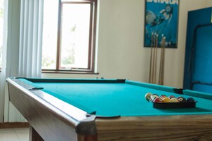 A pool table with balls and cues, a window with curtains, and a poster on the wall.