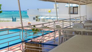 A pool area with a view of the ocean, a covered seating area, and a building with a striped awning. - Seacrest Beach Hotel (St. Ann's Bay)