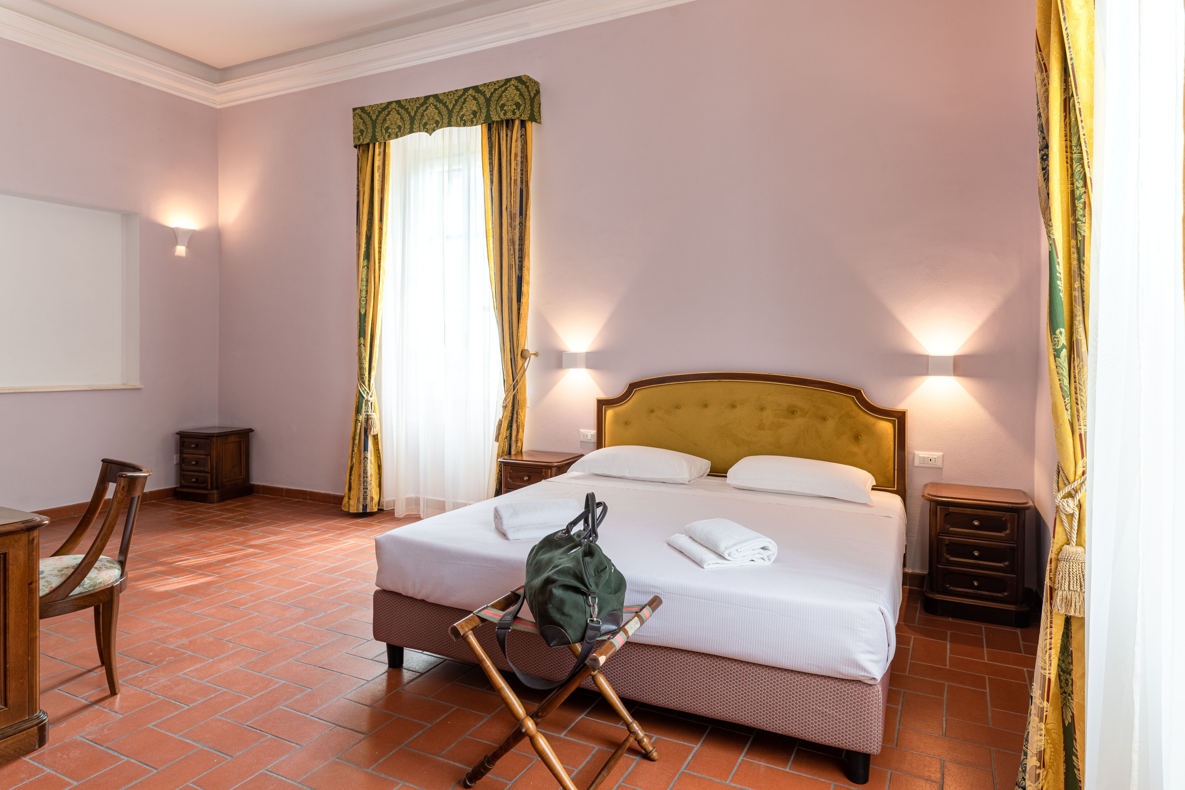 Une chambre d’hôtel bien rangée, avec un lit, des tables de chevet, une chaise, un bureau et une fenêtre avec des rideaux.