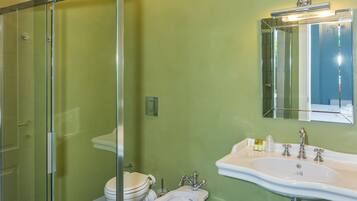A bathroom with a glass shower enclosure, two toilets, a bidet, a sink, and a mirror.