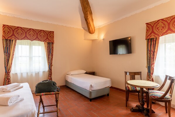 Una habitación de hotel con cama, una silla, una mesa, televisor y cortinas.