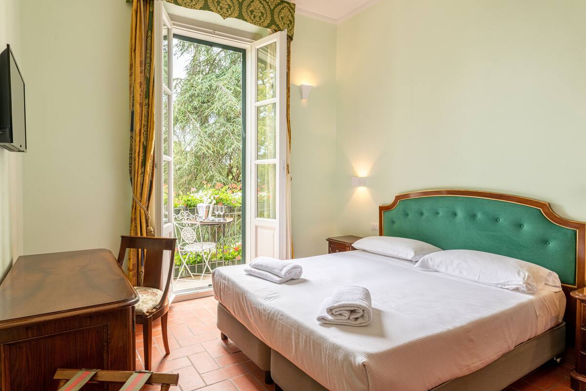A bedroom with a bed, a desk, a chair, and a window with curtains.