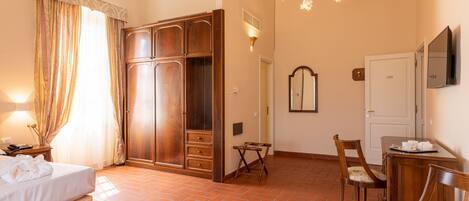 A hotel room with a bed, wardrobe, desk, chair, and a mirror.