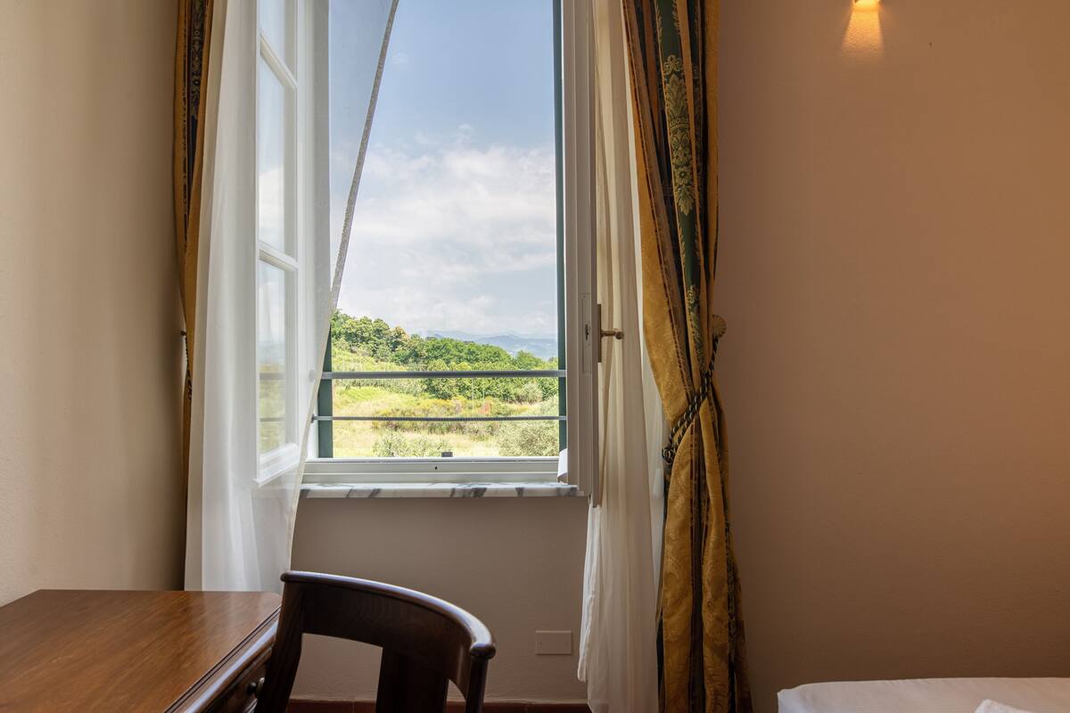A room with a wooden table and a chair, a bed, and a window with curtains.