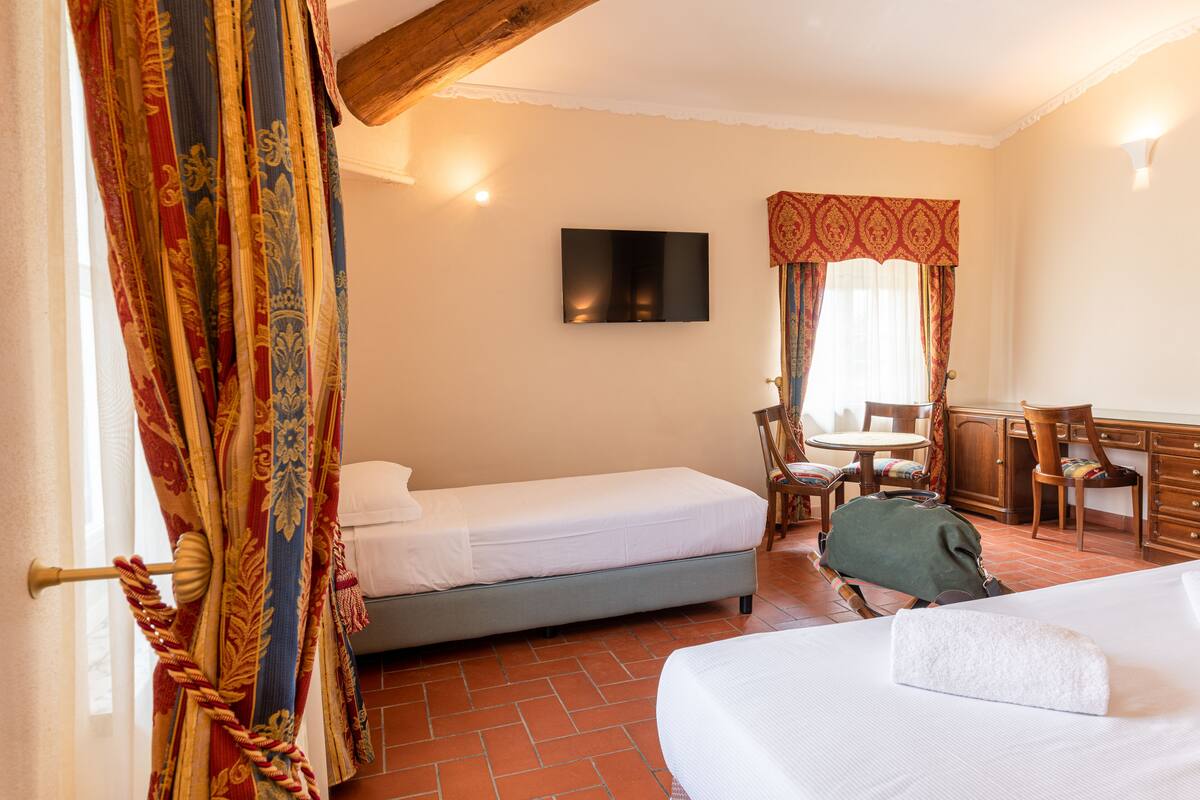 A hotel room with two beds, a TV, a desk with a chair, and a window with curtains.