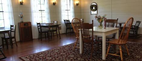 A dining area with a white table surrounded by wooden chairs, a patterned rug, and wall-mounted light fixtures.
