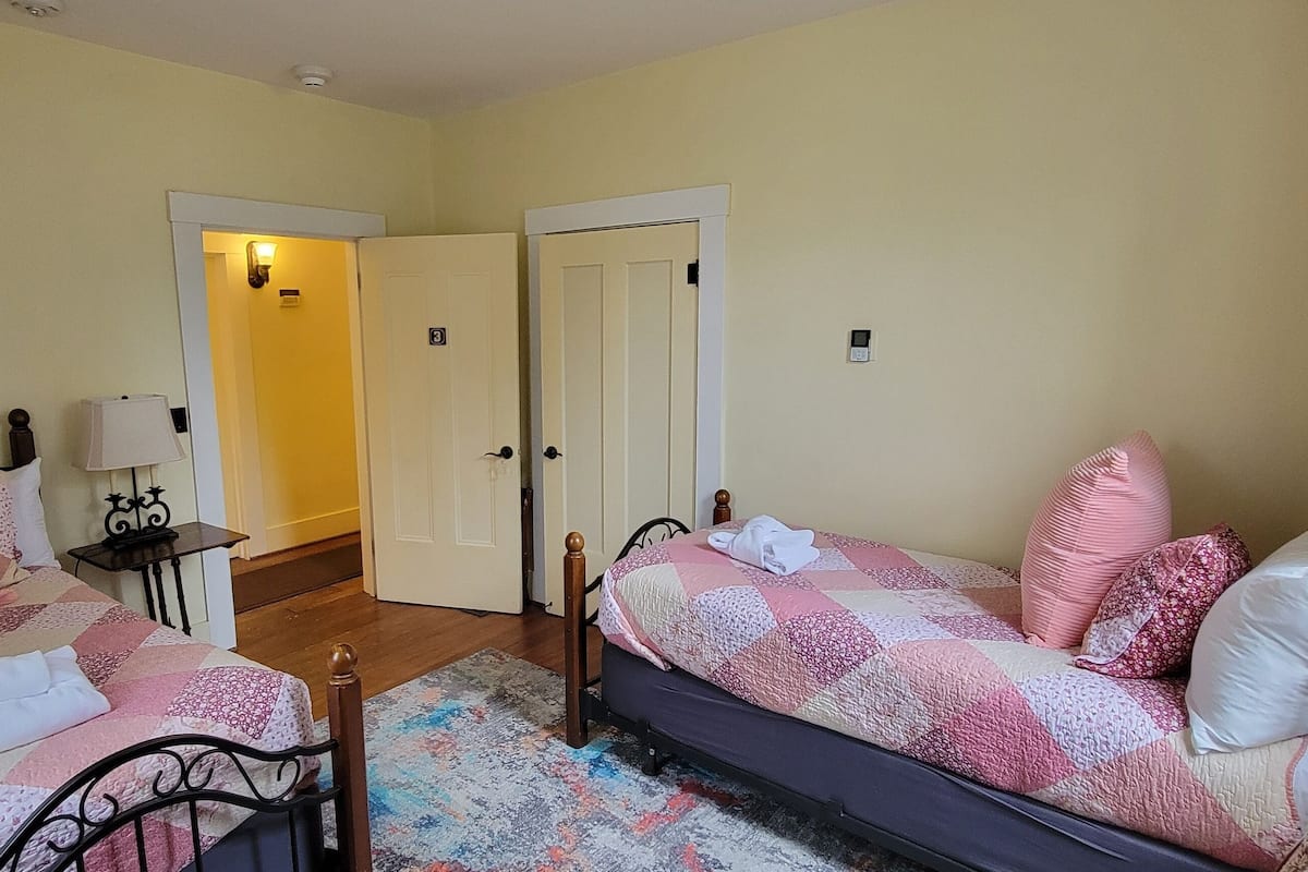 A bedroom with two beds, a nightstand, a lamp, and a door leading to another room.