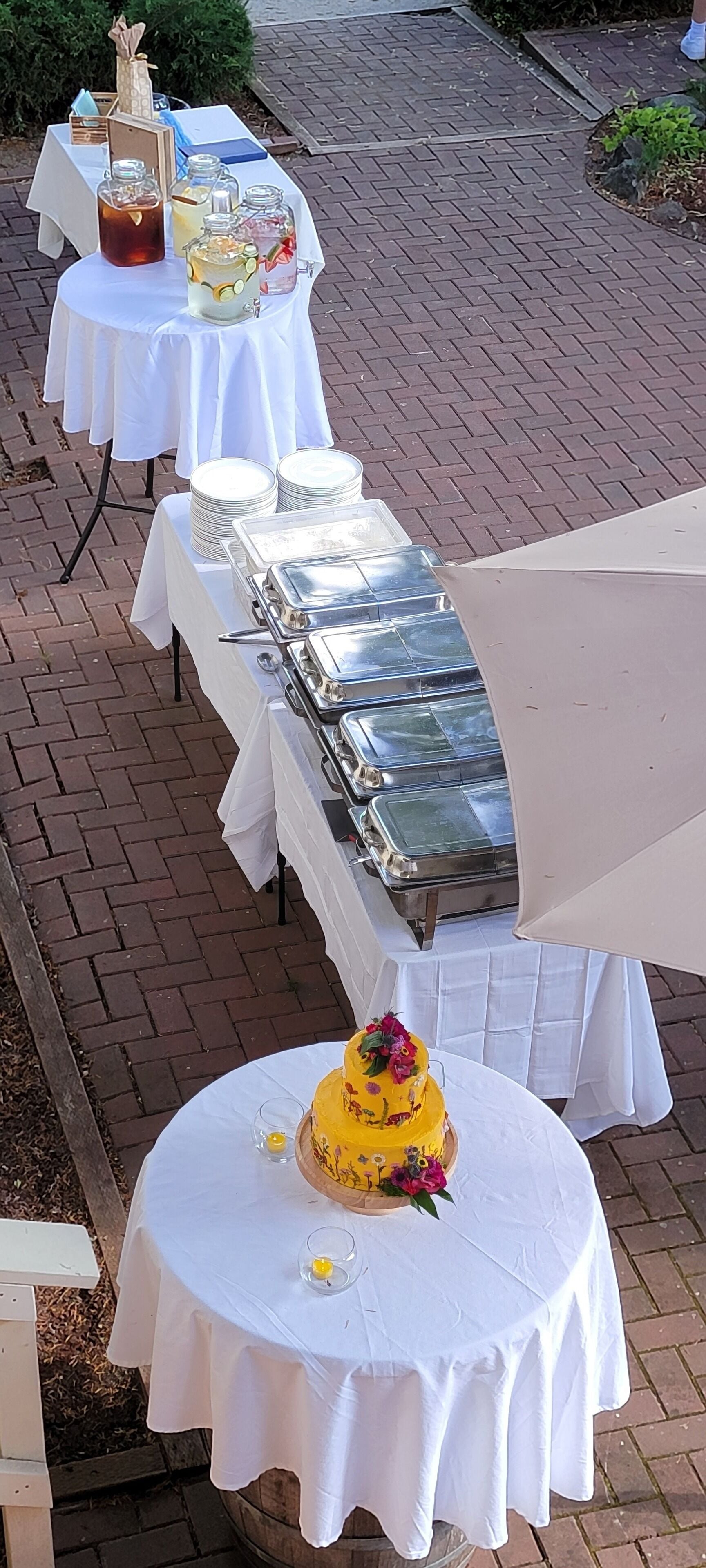 Een buffetopstelling met meerdere tafels, bedekt met witte tafelkleden, inclusief drank- en etensautomaat en een groot taartstuk als middelpunt.