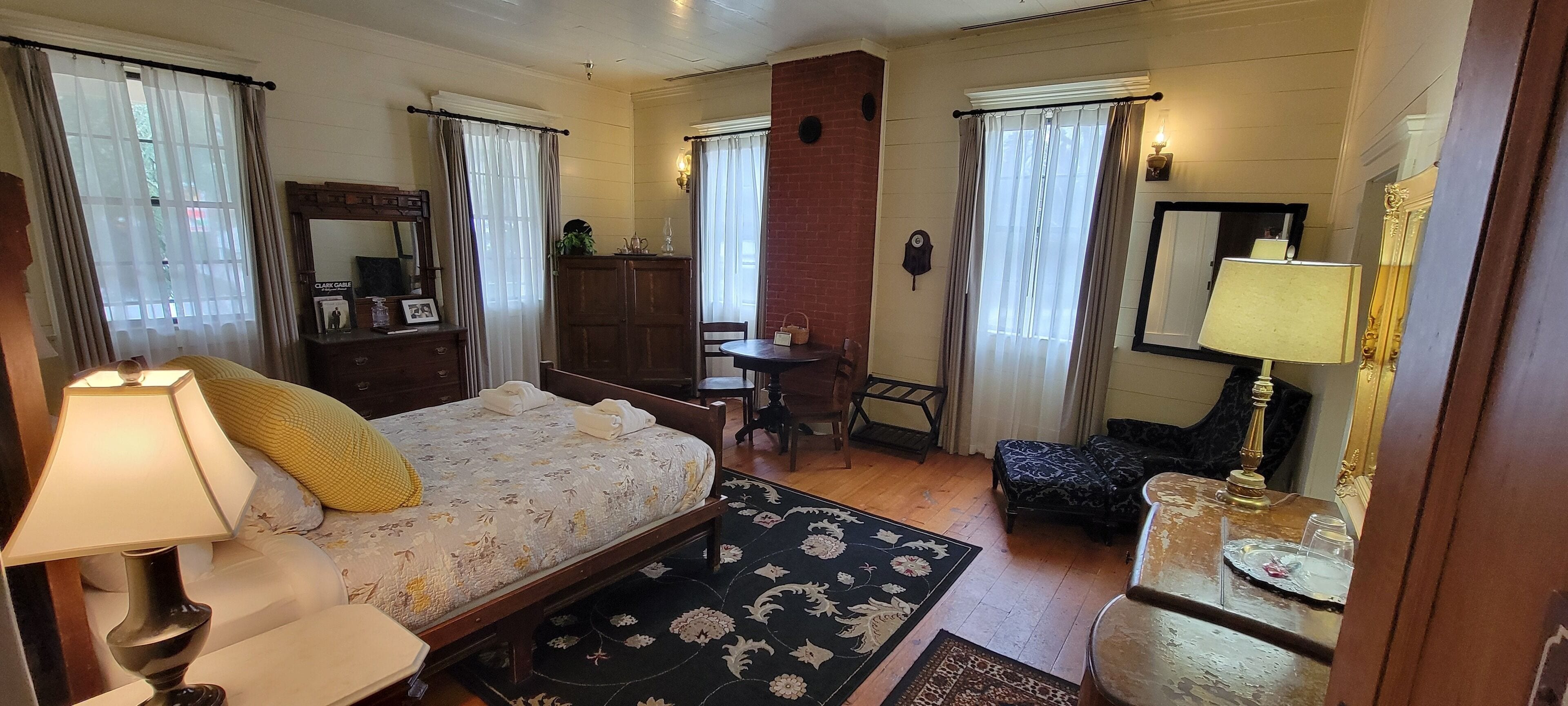 A hotel room with a bed, a desk, a chair, a small table with a lamp, and a mirror.