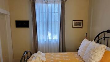 A single bed with a yellow floral bedspread, a black metal frame, and a patterned rug at the foot of the bed.
