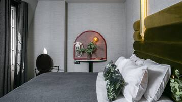 A hotel room with a bed, a desk with a telephone, a wall-mounted light, and a plant.