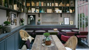 A cozy indoor seating area with a wooden table, wicker chairs, and a sofa. Shelves with books and decorative items line the walls. - La Planque Hôtel (Paris)
