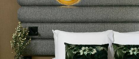 A hotel room with a large bed, a wall-mounted mirror, and a small side table with a vase of flowers.