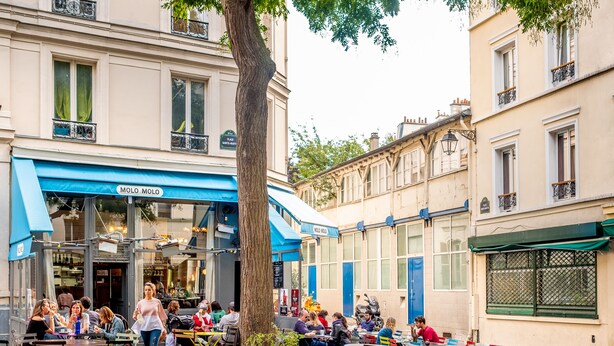 An outdoor café with tables and chairs, a tree, and buildings in the background. - La Planque Hôtel (Paris)