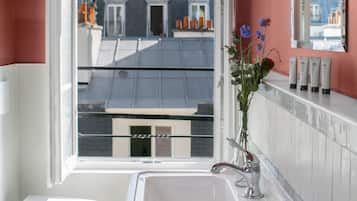 Un baño con un lavamanos blanco, un inodoro blanco, un espejo y una ventana con vistas a edificios.