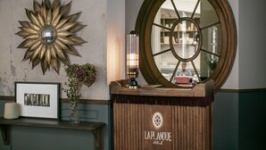 A reception desk with a framed photograph, a vase with flowers, and a large mirror with a wooden frame. - La Planque Hôtel (Paris)