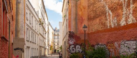 A narrow cobblestone street flanked by buildings with graffiti and a clear sky.