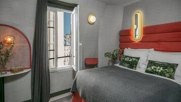 A modern bedroom with a large bed, a bedside table, a mirror, and a window with curtains.