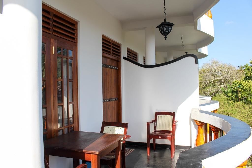 Un balcón con una mesa y sillas de madera, un farol colgante y una barandilla curva.