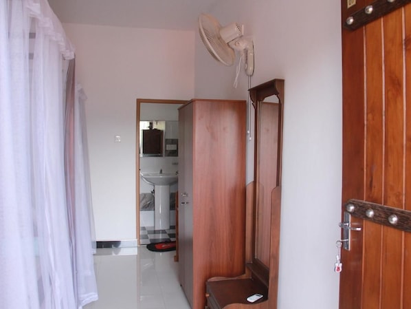 Habitación de hotel con un armario de madera, un espejo, un ventilador de techo y una puerta de madera.