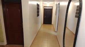 A narrow hallway with a wooden door at the end, tiled flooring, and a mirror on the right wall. - Imanisuites (Nairobi)