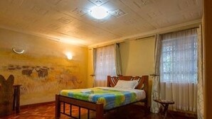 A room with a wooden bed, a small table, and a wall with a mural. - Imanisuites (Nairobi)