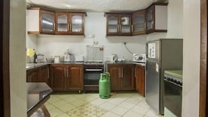 A compact kitchen with wooden cabinets, a gas stove, a microwave, and a refrigerator. - Imanisuites (Nairobi)