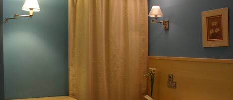A hotel room with two beds, a nightstand, a lamp, a curtain, and a framed picture on the wall.