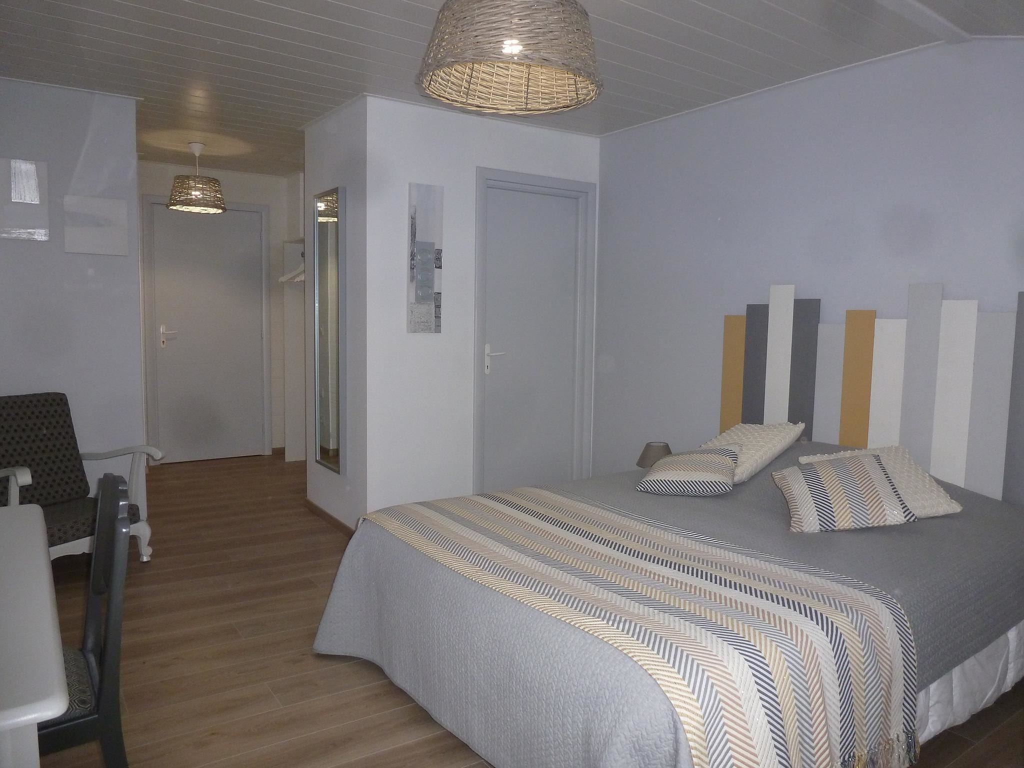 A bedroom with a bed, bedside tables, a chair, a hanging light fixture, and a door.