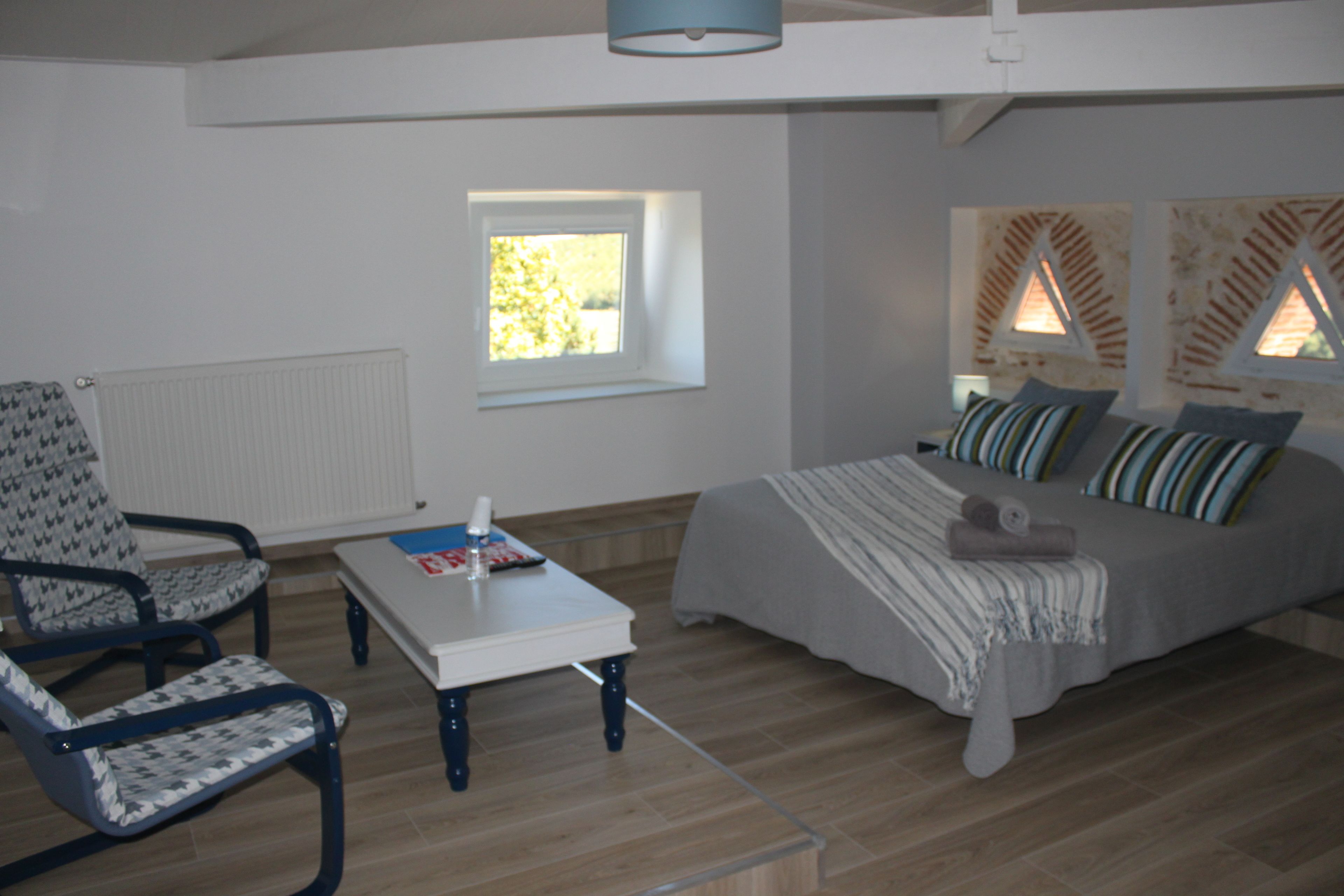 A bedroom with a bed, a chair, a table, and a window.