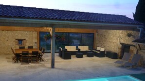 Un espace extérieur avec une piscine, une table et des chaises pour les repas, un coin salon avec des canapés et un mur en pierre.