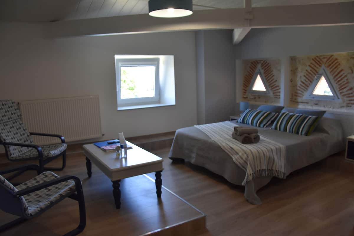 Une chambre à coucher avec un lit, une chaise, une table et une fenêtre.