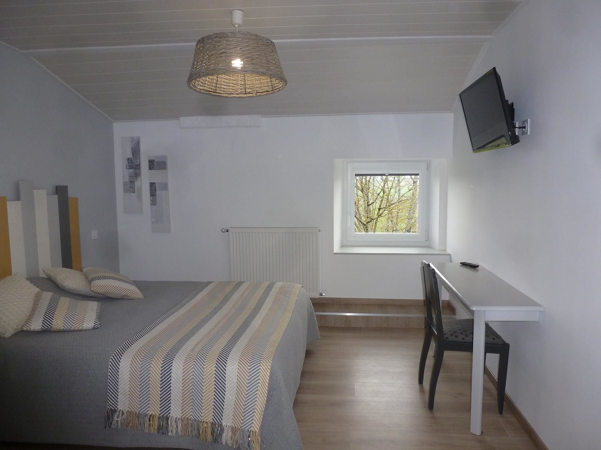 A bedroom with a bed, a desk, a chair, a television, and a window.