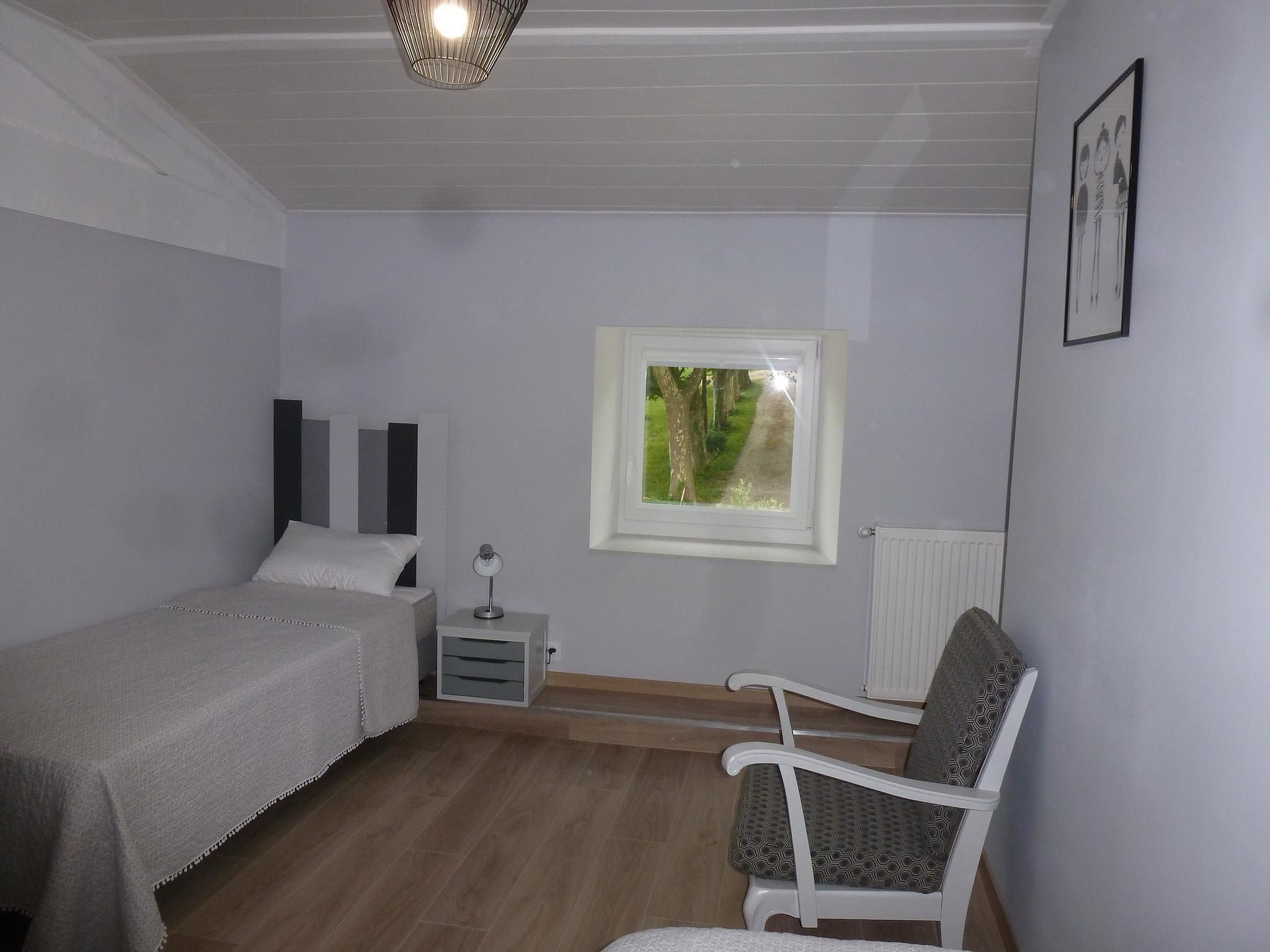 A bedroom with a bed, bedside table, chair, window, and radiator.