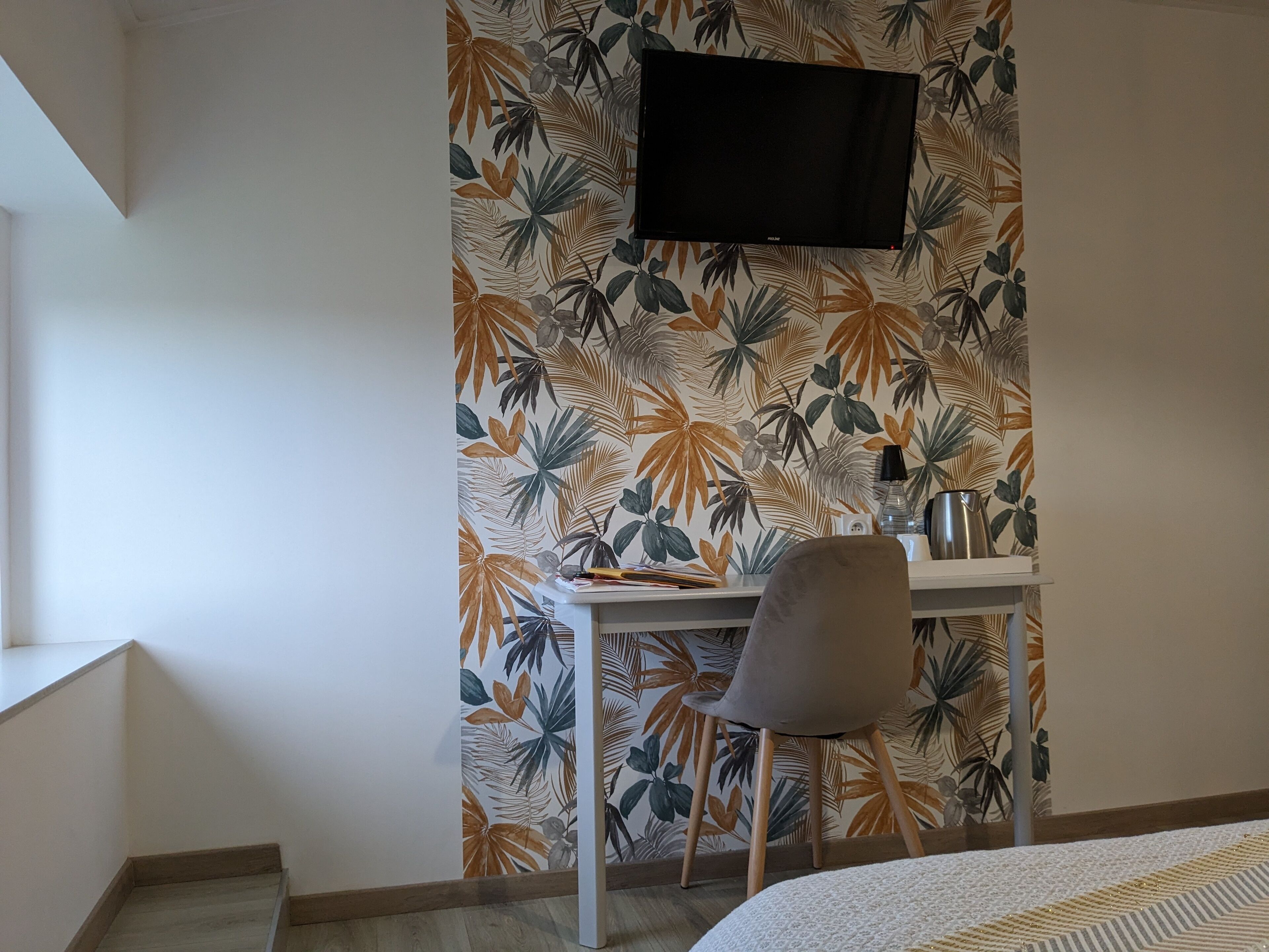 A room with a desk, chair, and a flat-screen TV mounted on the wall.
