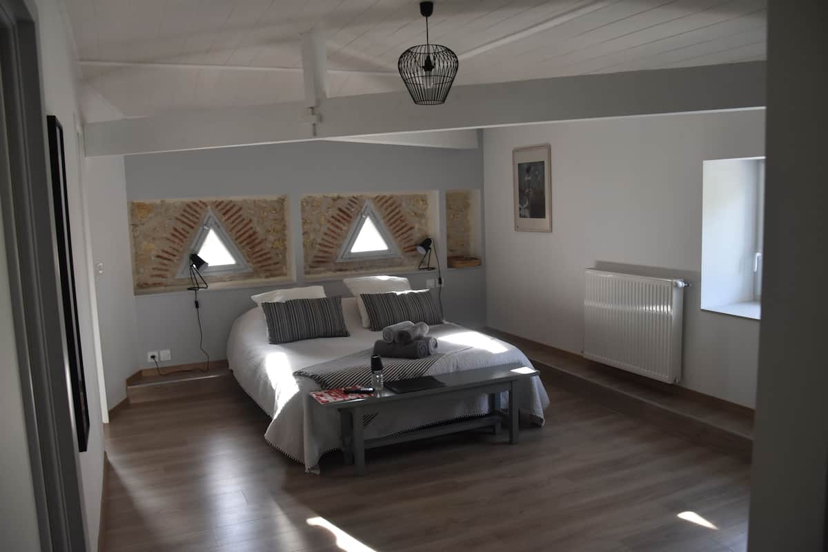 Une chambre à coucher avec un lit, des lampes de chevet, un radiateur et une fenêtre donnant sur l’extérieur.