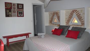 Een slaapkamer met een bed, rode en grijze kussens, een rode bank en een muur met ingelijste foto's.