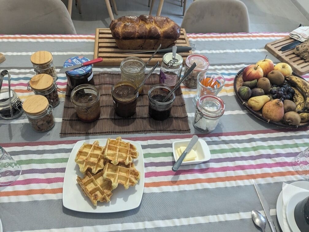 A breakfast table with waffles, jam, bread, and a fruit platter.