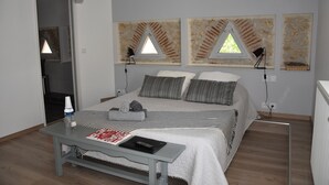 Une chambre à coucher avec un lit, des lampes de chevet, une table avec un livre et une fenêtre donnant sur un mur de briques.
