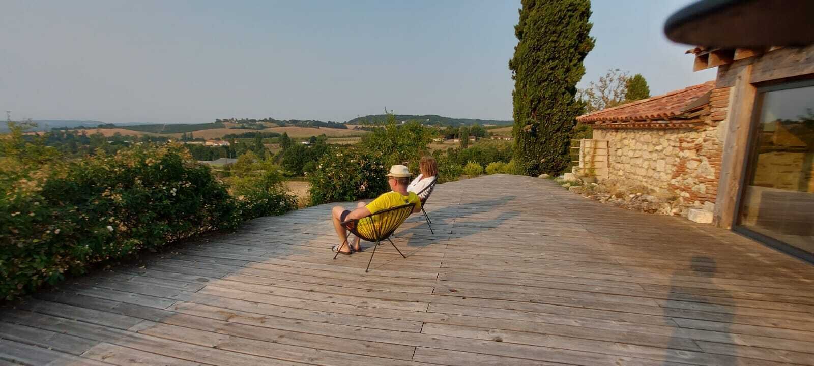 Una persona sentada en una silla hamaca en una terraza de madera con vistas a un viñedo.